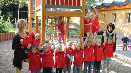 Passen perfekt: Die Mädchen und Jungen der Kita Spielkiste freuen sich gemeinsam mit Leiterin Ines Lüttig (l.)  und Elke Mißbach von KTSB Bau (r.) über die neuen T-Shirts.